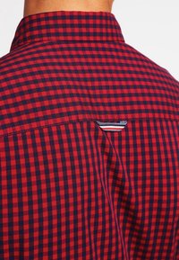 Rood en marineblauw geblokt shirt met een rug, een kraag en een kleine gestreepte stoflus onder de naad van de schouder.