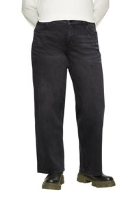 Schwarze Denim-Jeans, gerade geschnitten, verziert mit kleinen silbernen Nieten entlang der vorderen Taschen, kombiniert mit klobigen, schwarzer und grüner Stiefeln.