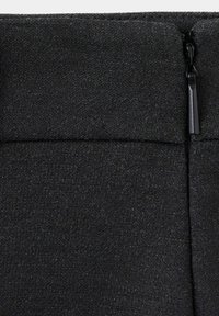Gros plan d'un tissu noir avec une fermeture éclair verticale et une couture cousue traversant horizontalement le dessus.