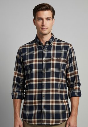 Camisa de cuadros en tonos marino con patrones en marrón y blanco, diseño de botones, mangas dobladas y un pequeño logo en el bolsillo del pecho.