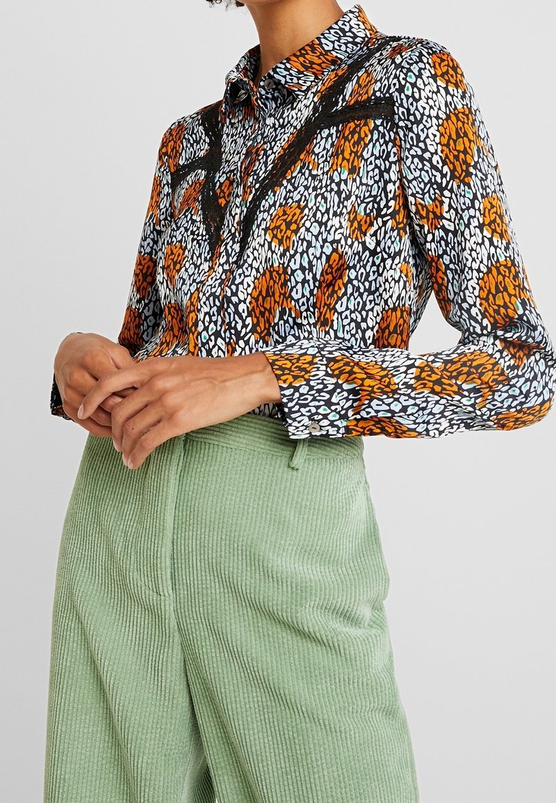 Camisa multicolor con estampado de animales en naranja y negro sobre un fondo blanco, con diseño de cuello y mangas largas.