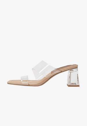 Sandales à talons transparents avec une tige en PVC transparent, une semelle beige, et un talon carré en acrylique. Présente un design minimaliste et une texture lisse.