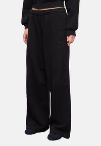 Zwarte wijde joggingbroek van zacht materiaal, met een elastische tailleband en subtiele geborduurde logo aan de voorkant.