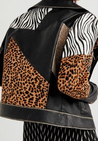 Giubbotto di pelle nera con stampa animale mista: righe di zebra e macchie di leopardo, finitura testurizzata e design a patchwork in contrasto.
