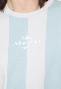 Světle modré a bílé pruhované bavlněné tričko s kulatým výstřihem, s potiskem "Nike Athletic Club 1972" v bílé barvě. Měkká textura.