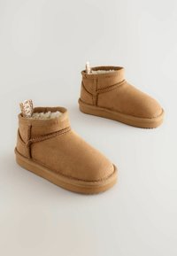 Bottines beige en daim douces avec une doublure pelucheuse, bout arrondi, accents cousus et une languette à l'arrière pour un enfilage facile.
