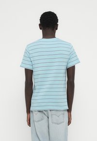 Ανοιχτό μπλε μπλουζάκι με οριζόντιες γκρι ρίγες, στρογγυλή λαιμόκοψη και κοντά μανίκια, κατασκευασμένο από μαλακό βαμβακερό ύφασμα. Εμφανίζεται η πίσω όψη.