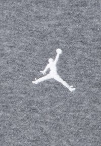 Gray fabric texture with a prominent white embroidered Jumpman logo in mid-air pose, showcasing smooth thread and clean design.