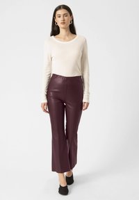 Bluză crem cu mânecă lungă, asortată cu pantaloni din piele ecologică borș cu talie înaltă, având picior evazat și o textură netedă. Pantofi moi negri completează ținuta.