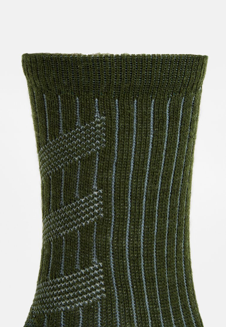 Grüner gestrickter Socke mit einem gerippten Muster. Besitzt hellblaue Streifen und ein strukturiertes Zickzack-Design am Körper. Glatte Garntextur.