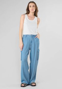 Pantaloni cargo a gamba larga di jeans di colore azzurro chiaro, con tasche laterali, abbinati a una maglietta senza maniche bianca e sandali neri.