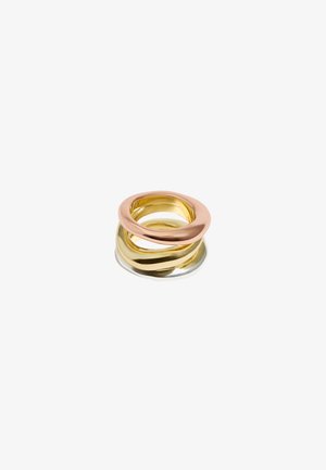 Three interlocking rings made of polished metal in gold, rose gold, and silver. Smooth, rounded shapes with reflective surfaces.