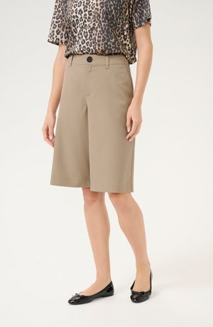 Khaki Bermuda shorts med en glat tekstur, med knaplukning og sidelommer, parret med en leopardprintet top og sorte flade sko.