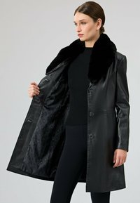 Czarny skórzany płaszcz z kołnierzem z sztucznego futra, jednozapięciowy fason i błyszczące wykończenie. Wnętrze ma wyściółkę w okrągły wzór.