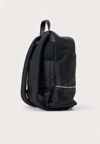 Juodas kuprinės krepšys su elegantišku dizainu, pasižymintis lygiu nailoniniu paviršiumi, tinklelio intarpais ir sidabriniu užtrauktuku šone.