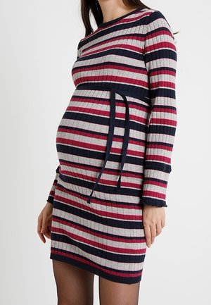 Schwangere Frau trägt ein langärmeliges, geripptes Strickkleid mit horizontalen Streifen in Marineblau, Pink und Grau sowie einem Taillenband.