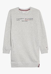 Harmaa huppari pitkillä hihoilla, pyöreällä kaula-aukolla ja sivutaskuilla. Varustettu tummansinisellä ja punaisella korostuksella "TOMMY HILFIGER NEW YORK" -tekstillä.