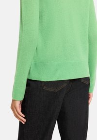 Pull vert clair avec une finition texturée, poignets et ourlet côtelés. Associé à un jean en denim foncé avec une coupe classique à cinq poches.