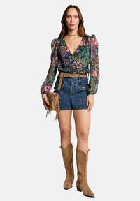 Blouse multicolore à motifs avec des manches bouffantes, associée à un short en denim taille haute. Les accessoires comprennent une ceinture beige et un sac à main.
