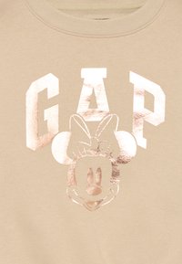 Beige sweatshirt med en glansig roséguldig "GAP"-logotyp och en tryckt design av Minnie Mouse med en rosett, på ett mjukt, texturerat tyg.