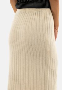 Gonna in maglia a costine beige, con strisce verticali e una vita aderente. La texture del tessuto appare morbida e calda, adatta per il clima fresco.