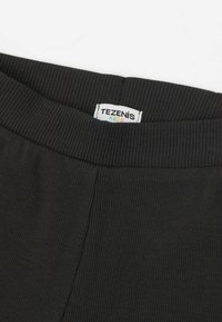 Černý ribovaný pásek z látky s plochými švy a štítkem s nápisem "TEZENIS KIDS", který ukazuje měkký, texturovaný povrch.