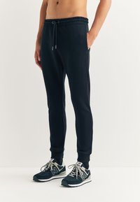 Zwarte joggingbroek met een elastische tailleband, zijzakken en geribbelde boorden. Gecombineerd met zwarte en grijze sportschoenen.