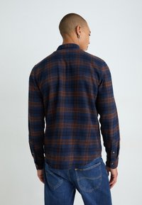 Navyblauwe en oranje geruite blouse met lange mouwen, knopenmanchetten en een kraag, gemaakt van zachte stof. Zichtbare stikdetails op de achterkant.