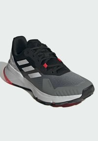 Zapatilla de running Adidas en negro y gris con rayas blancas, detalles en rojo en los cordones y una suela gruesa con amortiguación.