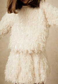 Ensemble deux pièces crème en peluche avec une surface texturée et duveteuse, orné de sequins, comprenant un haut ample et une jupe assortie.