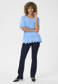 Svijetloplava pletena majica s kratkim rukavima i valovitim rubom; uparena s tamnoplavim trapericama sa širom nogavicom i crnim štiklama s ošiljenim vrhom.