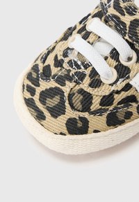 Καμβαδένιο αθλητικό παπούτσι με λεοπάρ σχέδιο, λευκά κορδόνια, υφή επιφάνειας, στρογγυλή μύτη και αντίθετη λαστιχένια σόλα σε φυσικό χρώμα.