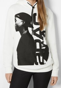 Sudadera blanca con estampado gráfico negro que presenta dos perfiles y el texto "2PAC". Capucha con cordones y puños acanalados, con un corte holgado.