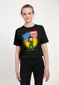 Schwarzes T-Shirt mit einem Cartoon-Charakter in einem grünen Outfit, der salutiert und eine blau-rot gestreifte Flagge mit Sternen hält, vor einem gelben Burst.