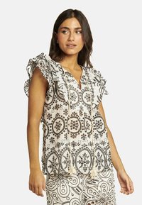 Blusa blanca con estampados florales y de cachemira en negro, mangas con volantes y escote en V, con detalles en borlas en la parte frontal.