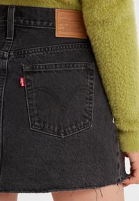 Zwarte spijkerrok met een rafelige zoom, voorzien van een achterzak en een bruine leren label met branding op de taille.