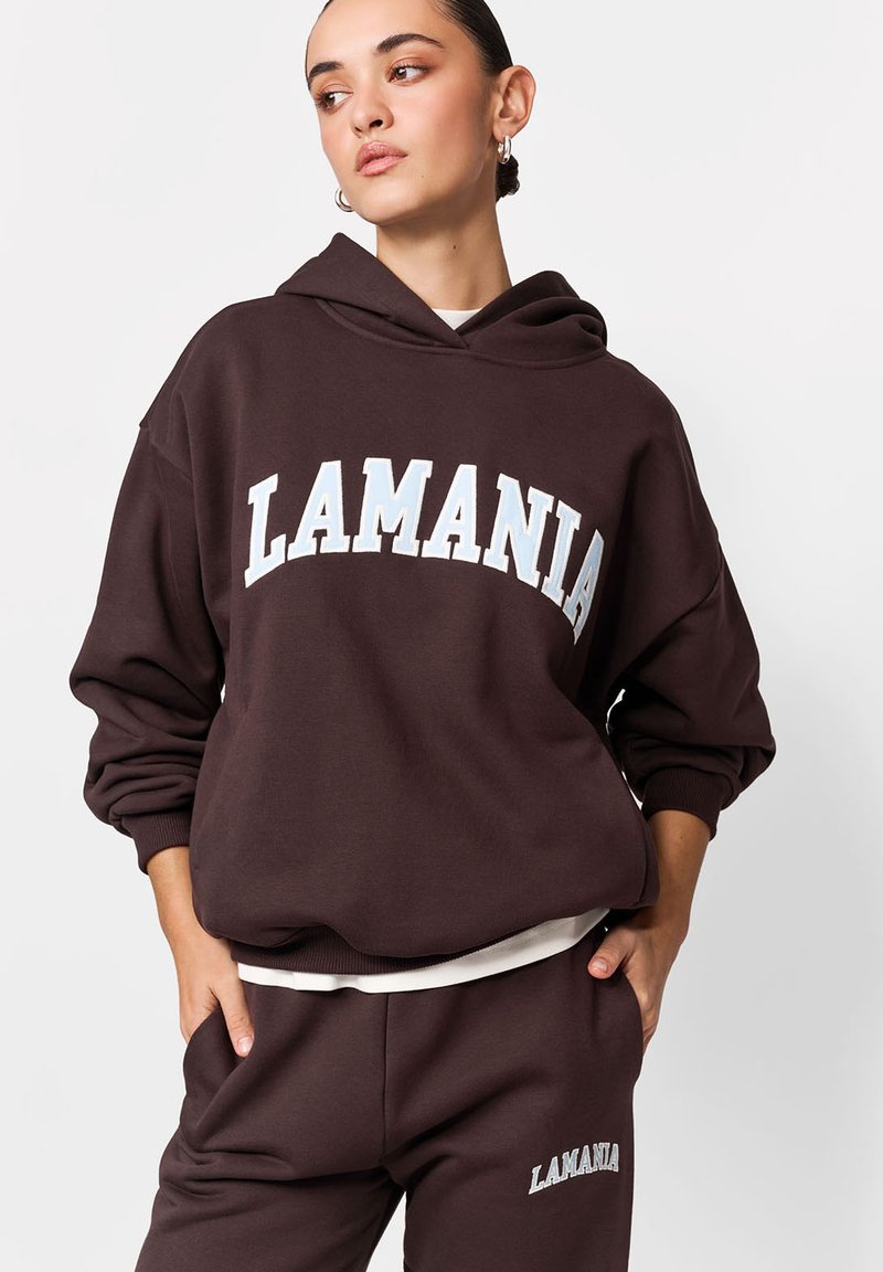 Hanorac maro cu glugă, cu inscripția "LAMANIA" imprimată alb pe piept. Croială lejeră, cu manșete rib și textură moale.