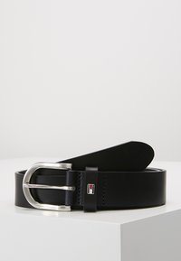 Svart läderbälte med en silverfärgad metallspänne och logotypaccent. Designen är slät, med enkel söm och rundad ände.