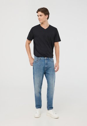 Maglietta nera a scollo a V, jeans azzurri chiari e sneakers bianche. La maglietta ha maniche corte e i jeans hanno un taglio dritto con dettagli scoloriti.