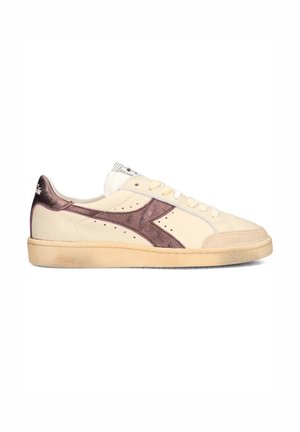 Sneaker crema basse con logo laterale metallizzato viola, davanti con lacci e suola beige leggermente usurata, inclinata verso sinistra su sfondo bianco.