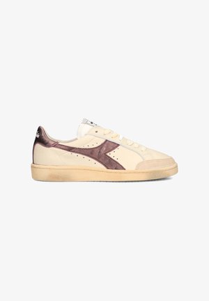 Sneaker crema basse con logo laterale metallizzato viola, davanti con lacci e suola beige leggermente usurata, inclinata verso sinistra su sfondo bianco.