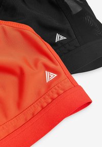 Svarta och orangea idrottsshorts tillverkade av ett mjukt och lätt tyg. Har vita logotypdetaljer och kontrasterande sömnadsdetaljer.