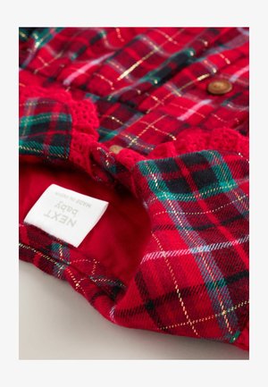 Röd rutig tyg med gröna och gyllene accenter, texturerad krage med spetskant och träknappar. Etikett med texten "NEXT Baby."