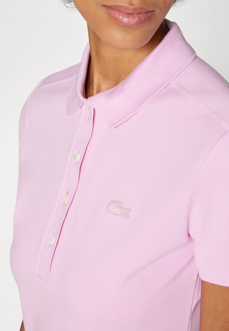 Camiseta polo rosa con una superficie texturizada, con cuello clásico, tapeta de tres botones y un logotipo bordado en el lado izquierdo del pecho.