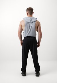 Top cinza sem mangas com capuz e um corte solto, combinado com calças de desporto pretas com riscas laterais e um design de perna afunilada.