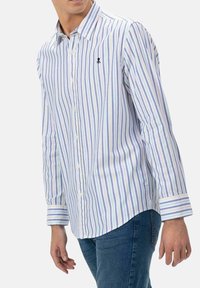 Camisa de botones con rayas verticales en azul, púrpura y blanco. Hecha de una tela suave, con cuello y logo en el pecho.