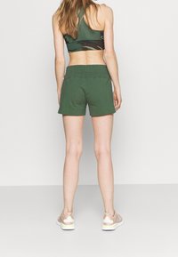 Pantalones cortos de algodón verde con una cintura elástica, un ajuste relajado y franjas laterales, combinados con un sujetador deportivo con estampado y zapatillas ligeras.