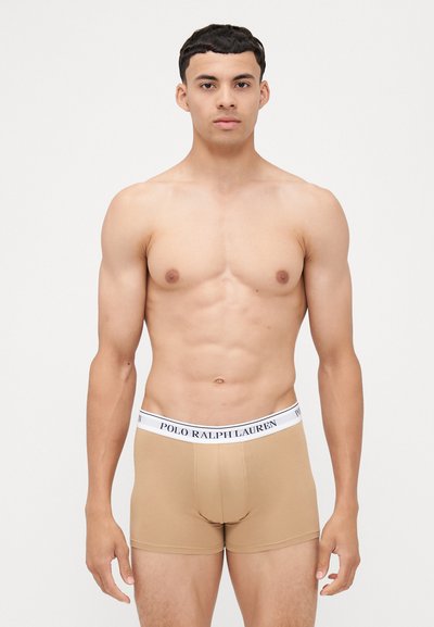 Bež bokserice z belim pasom, na katerem je napis "POLO RALPH LAUREN" v mornarsko modri barvi, izdelane iz gladkega, raztegljivega materiala.