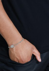 Sølvarmbånd med kjedesdesign som har runde elementer og et rundt vedheng. Båret på håndleddet, som fremhever en glatt metallisk finish.