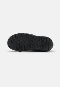 Sorte sneakersåle med et struktureret grebmønster med hexagonale former, hævede linjer og en afrundet hæl.